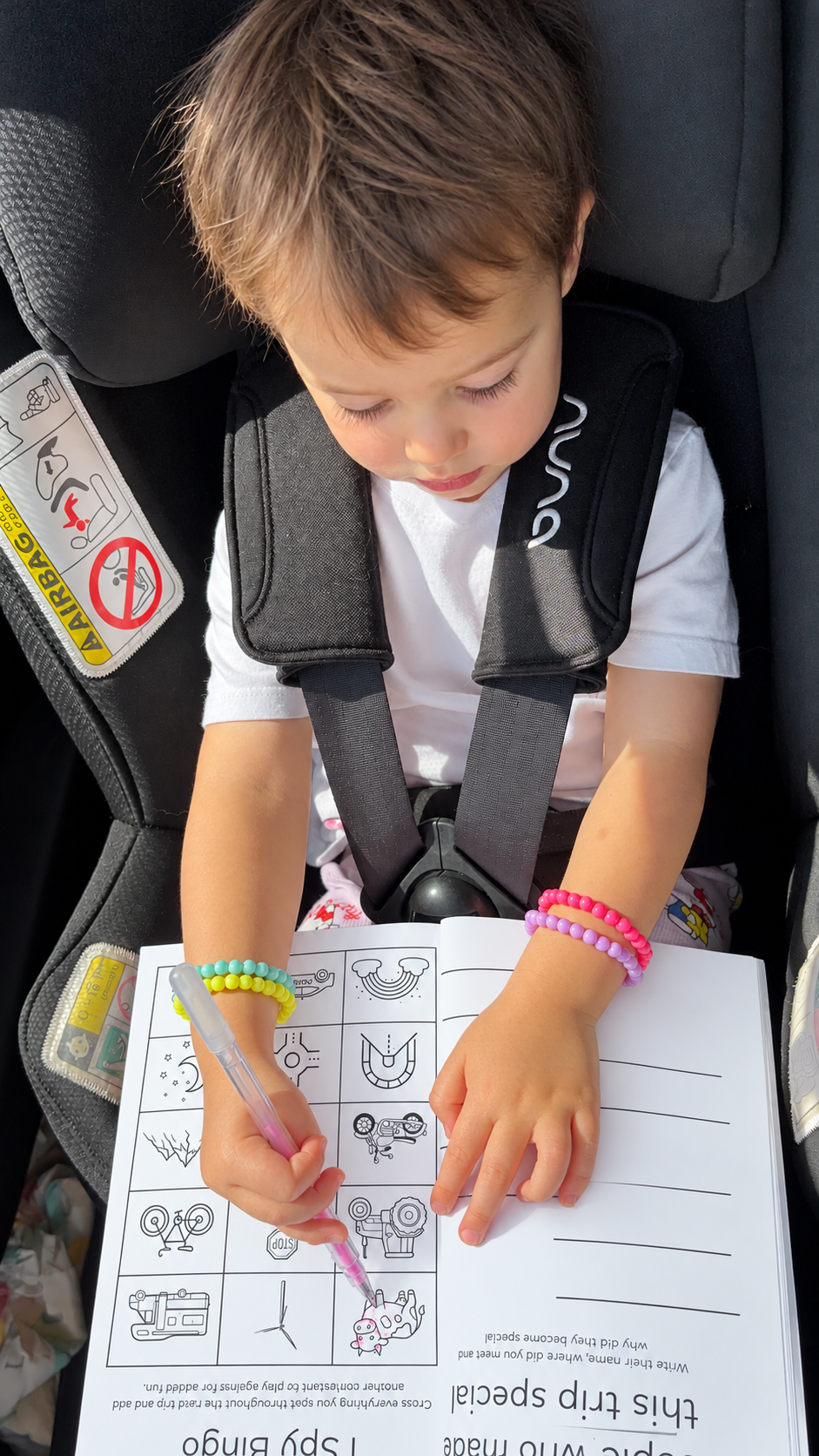 Child filling in I Spy Bingo in the Road Trip Logbook in a car seat